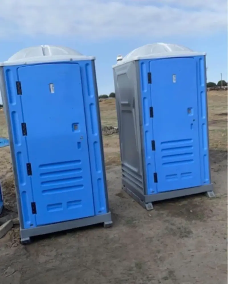 Two blue porta potties on a dirt construction site