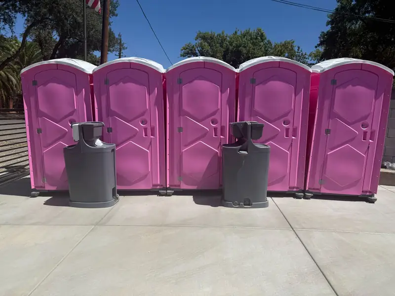 A row of five pink porta potties with two handwashing stations