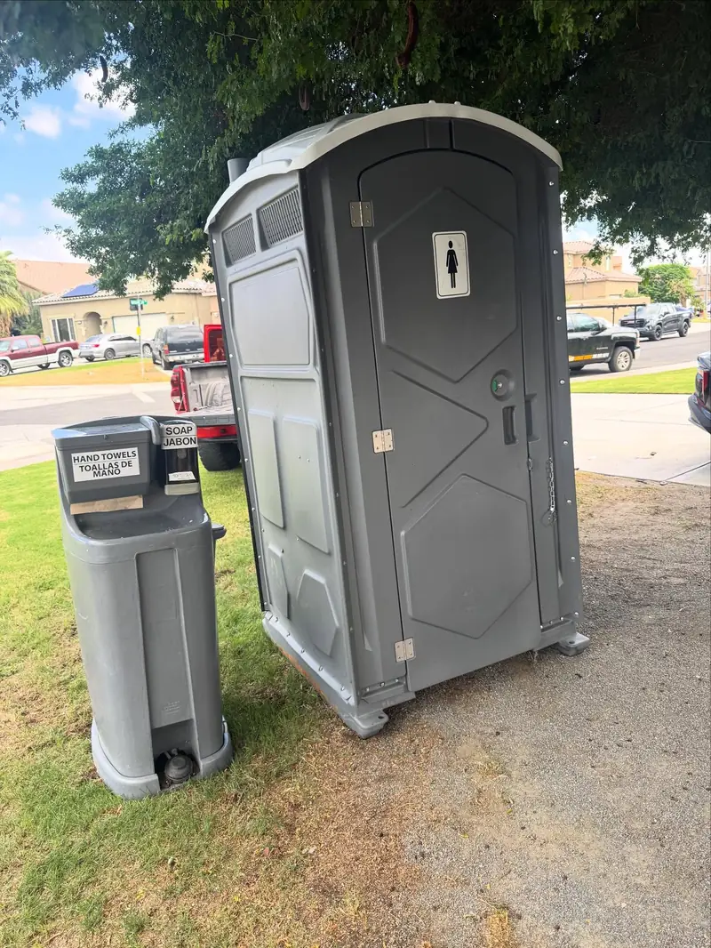 A gray portable toilet beside a gray handwashing station