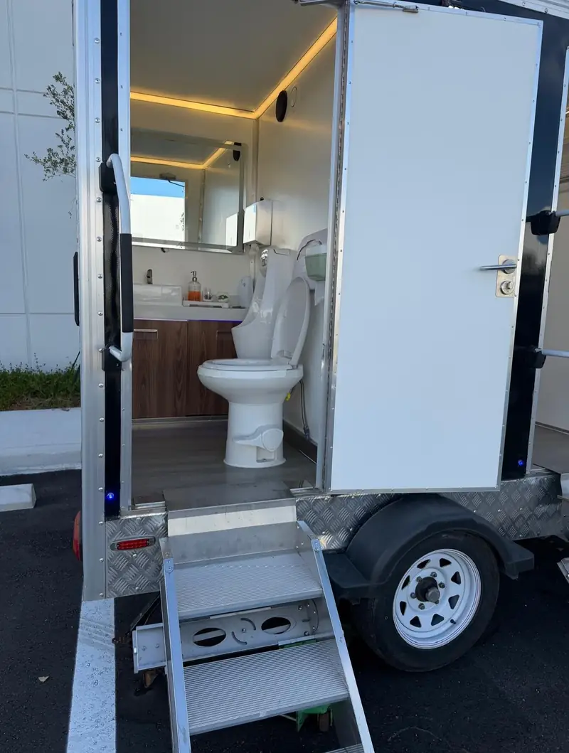 Inside a restroom trailer with a wood vanity and a flushing toilet