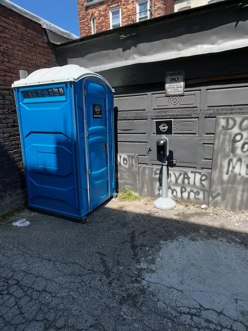 A blue porta potty in a narrow space next to a building