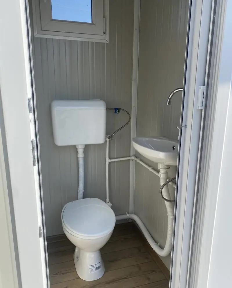 Ceramic toilet and small sink inside a white VIP restroom unit